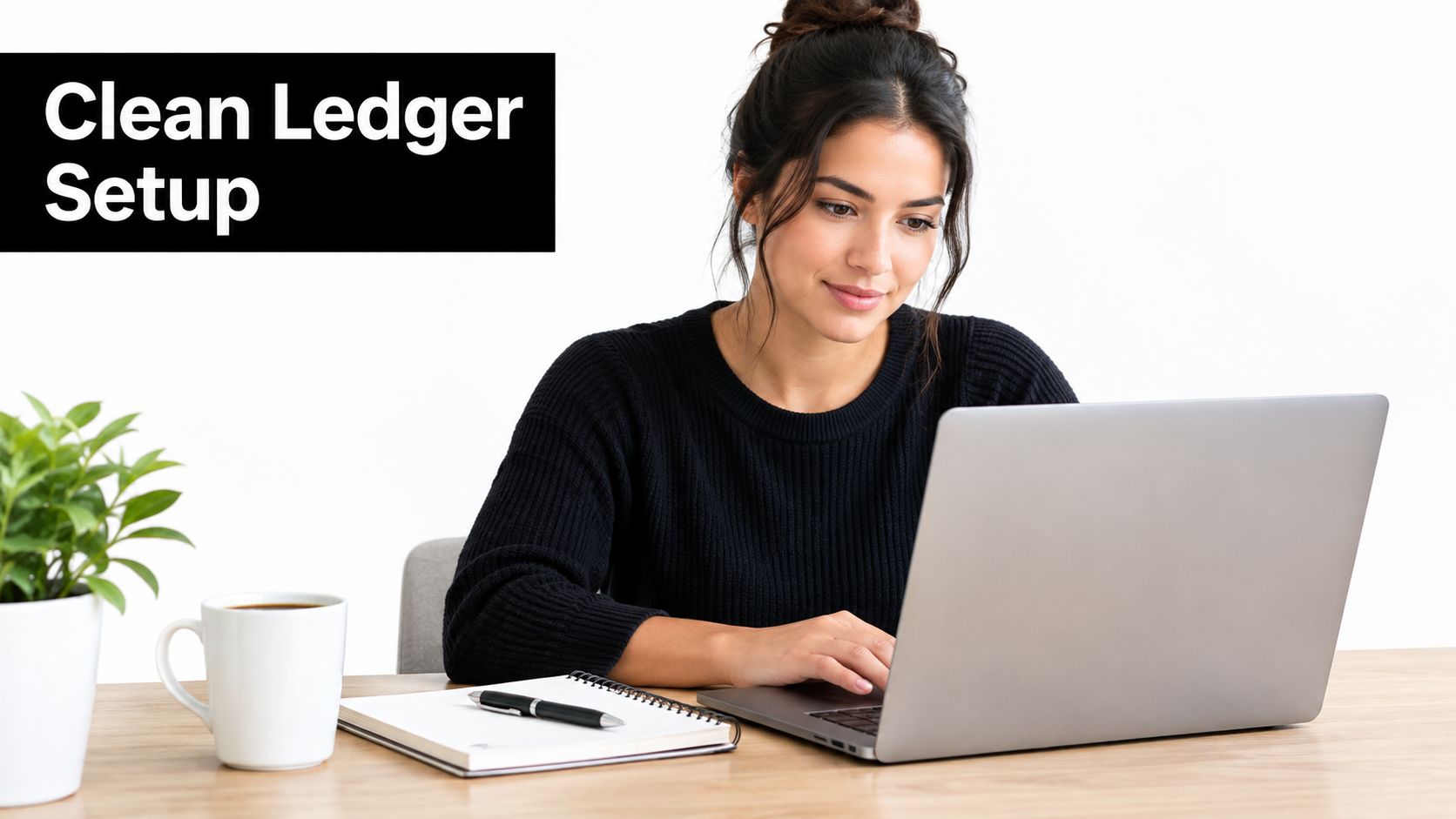 A woman working on a laptop at a wooden desk with a plant, coffee mug, and notebook.
