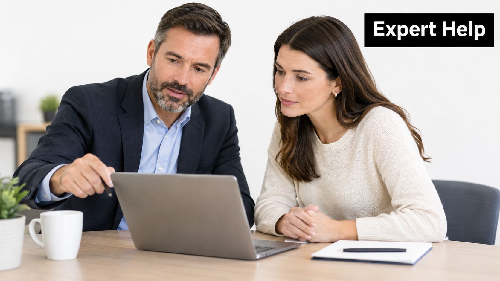 A professional man and woman sitting at a desk reviewing financial documents on a laptop computer together.